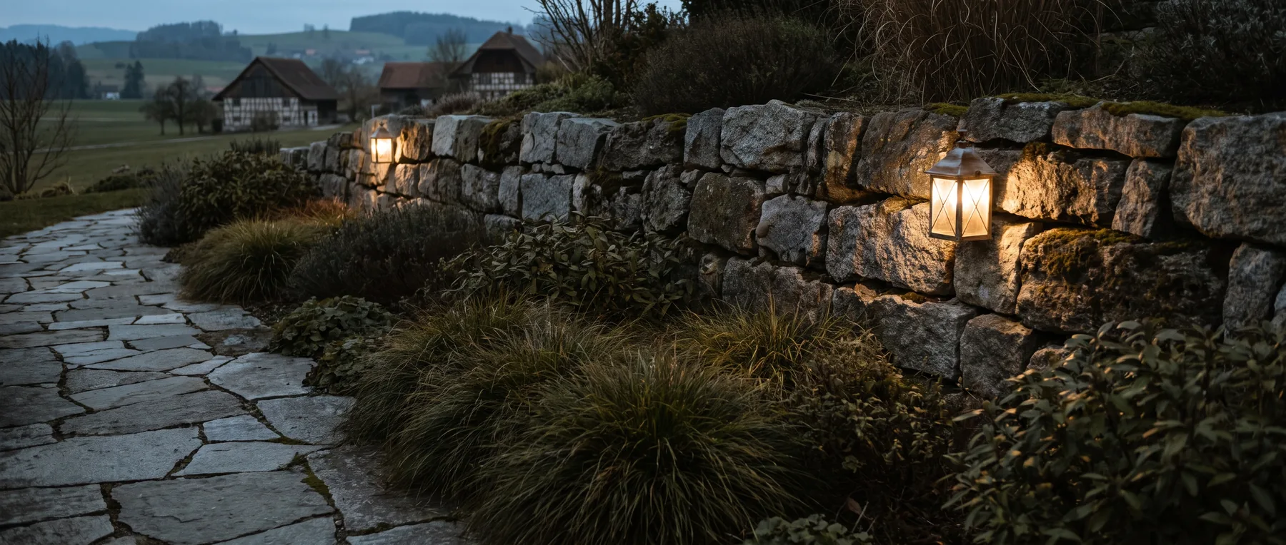Niedrige Wegleuchten in der Dämmerung, warmes Streiflicht auf einer Natursteinmauer