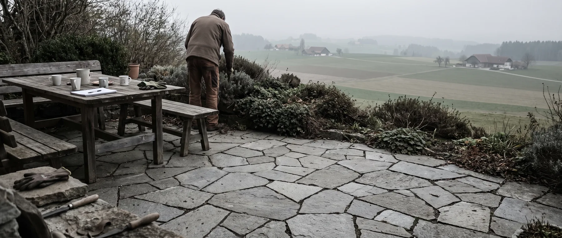 Natursteinterrasse mit engen Fugen, schlichtem Gartentisch und niedriger Randbepflanzung